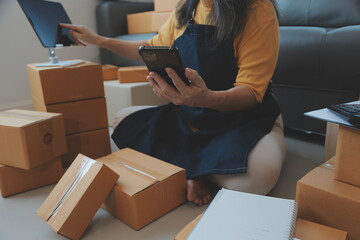 Startup SME small business entrepreneur of freelance Asian woman wearing apron using laptop and box to receive and review orders online to prepare to pack sell to customers, online sme business ideas.