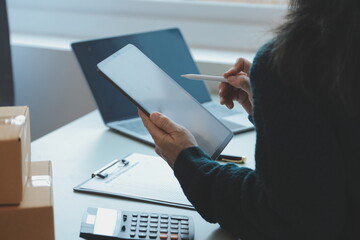 Startup SME small business entrepreneur of freelance Asian woman wearing apron using laptop and box to receive and review orders online to prepare to pack sell to customers, online sme business ideas.