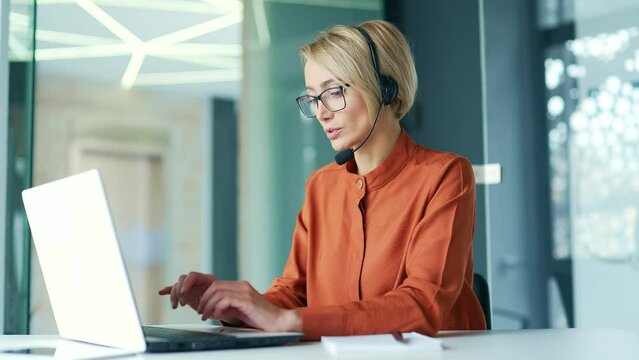 Сorporate operator who works in the support service speaks on a video call using a laptop. Сall center agent in a wireless headset helps a customer with a complaint in a office by answering questions