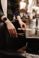 Hair style, hairdresser, beauty and customer service concept. Cropped shot of barber man hands hold professional stylish gold hairbrush and scissors by the workplace, leather black chair in barbershop