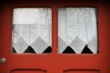 Alte rotbraune Holztür von Wohnhaus mit Glasfenster und weißen Gardinen
