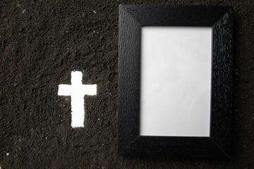top view of picture frame with white cross shape on dark soil death grim reaper funeral
