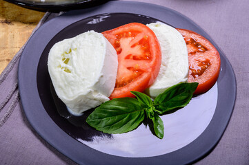Sliced white ball of Italian soft cheese Mozzarella di Bufala Campana served with fresh green basil and red tomato