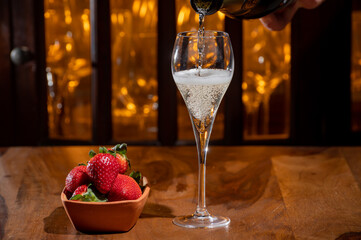 Glass of brut champagne bubbles wine in tulip glass and bowl with fresh strawberries on evening bar lights background