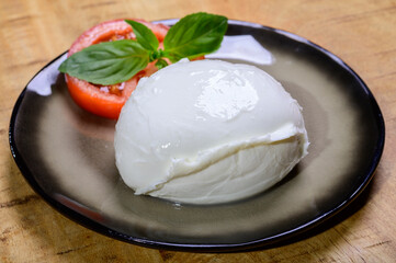 White ball of Italian soft cheese Mozzarella di Bufala Campana served with fresh green basil and red tomato