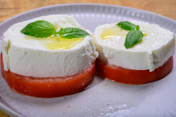 Sliced white ball of Italian soft cheese Mozzarella di Bufala Campana served with fresh green basil and red tomato