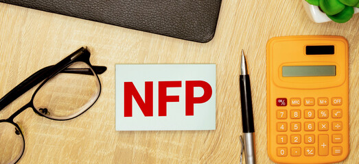 Selective focus of pens, clock, money banknote and notebook written with text NFP stands for Nonfarm payrolls.