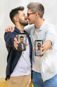Happy homosexual men hugging and showing smartphones on street