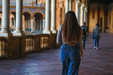 Fototapeta na wymiar Back view of a young woman visiting Spain Square (Plaza de Espana). Seville tour. Spanish Square, a beautiful famous tourist place.