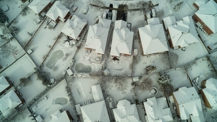 Looking down from an aerial view at houses, streets and backyards in the suburbs during winter