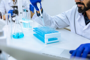 Fototapeta premium Scientist holds glass-dropper with reagents makes notes in laptop, experimenting with medical sample