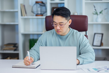 young man working on laptop in modern office, writing notes.