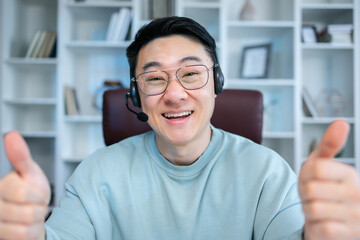 Cheerful happy adult asian guy showing like thumb up hands at camera, smiling, laughing, speaking on video conference call. Satisfied customer, user head shot portrait.