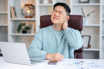 Obraz premium Exhausted young male worker sit at desk massage neck suffer from strain spasm muscles.