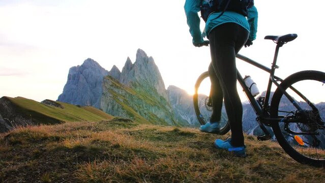 Young man with mountain bike walking on Seceda mountain peak at sunrise. Puez Odle, Trentino, Dolomites, Italy.