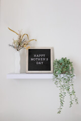 Happy Mother's Day lettering on a black and tan letter board sitting on a floating shelf with...