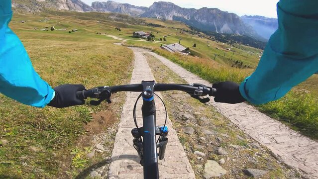 POV shot man with mountain bike cycling down Seceda mountain on dirt road. Puez Odle, Trentino, Dolomites, Italy.