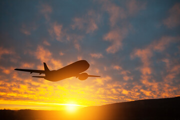 Fototapeta na wymiar Airplane taking off at the sunset sky. Silhouette of aircraft in the sky.
