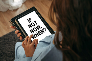 A woman holds a tablet in her hands on the screen of which it is written - If Not Now, When