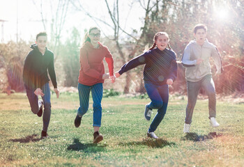 Group of cheerful teenagers running together in spring city park. Happy healthy youth concept