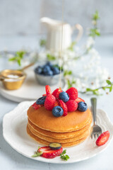 Pancakes served on a white plate with fresh fruit