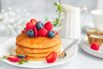 Pancakes served on a white plate with fresh fruit.