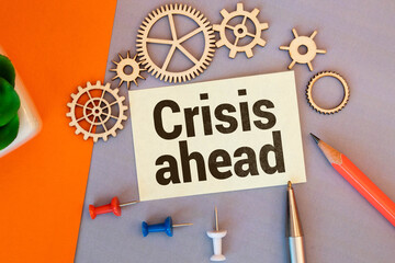 On a light-colored office table is a computer, a black calculator, a pen, and a notebook with the text CRISIS AHEAD