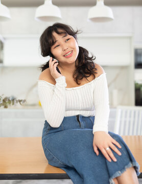 Young girl cheerfully chatting on a mobile phone while sitting on a table in a home interior