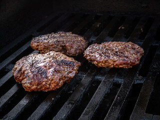 Three homemade hamburgers on the barbeque grill.