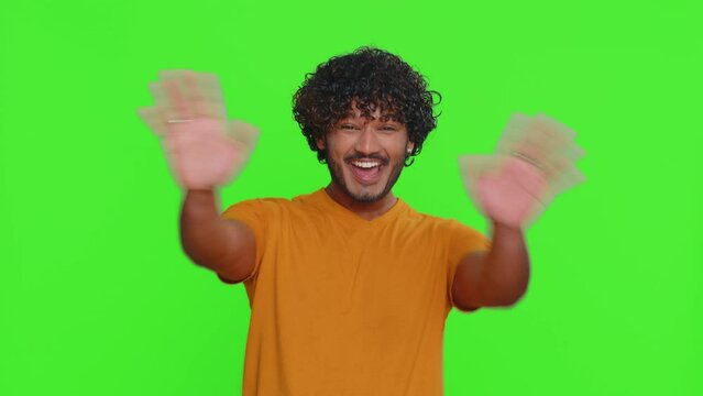 Young indian man appearing from below and waves hand palm in hello gesture welcomes someone with hospitable expression expresses positive emotions. Hindu guy isolated on green chroma key background