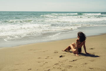 Fototapeta na wymiar beautiful brunette girl sits on the sand on the beach in front of the sea