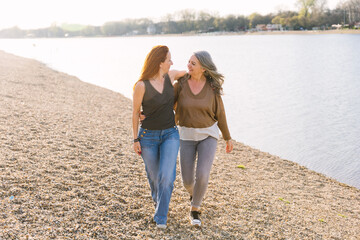 Elderly gray-haired mother and adult daughter walking along the beach together. The concept of taking care of an elderly mother