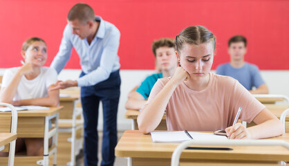 Fototapeta na wymiar Portrait of focused teenage schoolgirl writing lectures in workbooks in classroom during lesson..