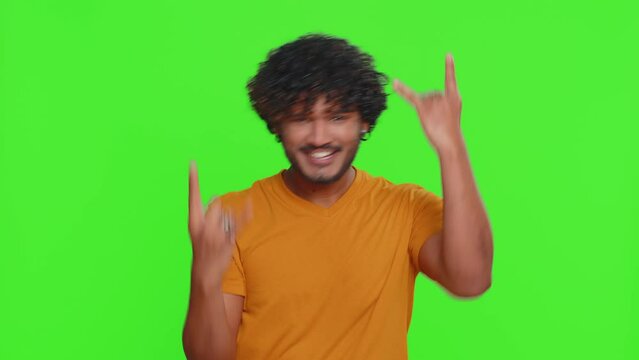Overjoyed young indian man showing rock n roll gesture by hands, cool sign, shouting yeah with crazy expression, dancing, emotionally rejoicing in success. Hindu guy isolated on chroma key background