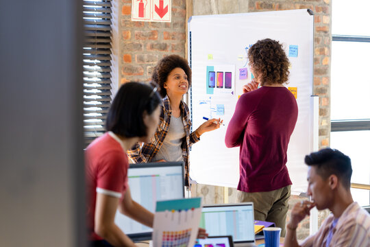 Happy diverse designers discussing project at whiteboard in busy casual office