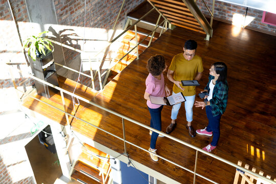 High angle of diverse creative colleagues using tablet and discussing in office corridor, copy space
