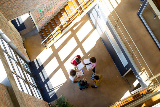High angle of diverse creative colleagues using tablet and discussing in office corridor, copy space