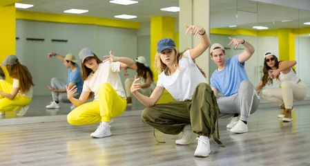 Door stickers Dance School Group portrait of talented active tween dancers in casual clothes squatting and learning new dance move in hall