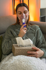 A 40-year-old woman inhales with a nebulizer while sitting on the couch Treatment of the...