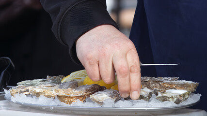 Chef at farmers street food market serves a portion of oysters with lemon on ice chips for his customer.