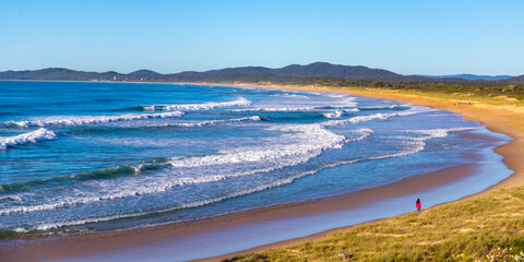 beautiful long haired girl walking on wooli beach during sunrise; long beach with large waves on the coast of pacific in yuraygir national park, new south wales, australia
