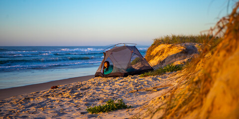 A beautiful girl admires a wonderful sunrise on the beach from her tent. Camping on the beach in...