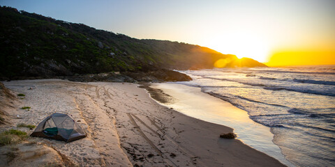 A beautiful girl admires a wonderful sunrise on the beach from her tent. Camping on the beach in Australia, Hat Head National Park, NSW