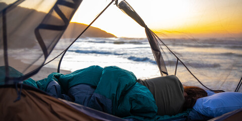 A beautiful girl admires a wonderful sunrise on the beach from transparent tent. Camping on the...