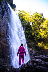 close up on a beautiful, brave, long haired girl standing in front of a large waterfall in australian rainforest, red cedar falls in dorrigo national park, new south wales, between brisbane and sydney