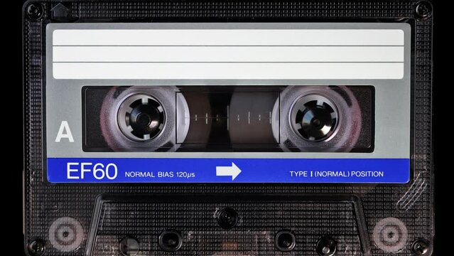 Audio cassette tape in use for sound recording in the tape recorder. A vintage, blue, brand new blank labelled music cassette playing back in a deck player. Static video camera shot. Close up, 4K
