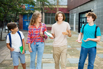 School friends, a girl and three boys with school backpacks on their backs, walk after class