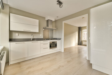 a kitchen with white cabinets and wood flooring in the middle of the room, there is an open door that leads to another