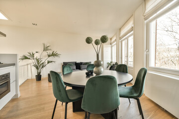 a dining room with green chairs and a round table in front of a large window that looks out onto the street