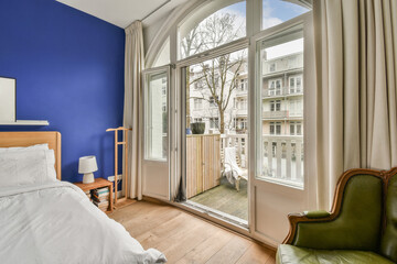 a bedroom with blue walls and white bedding, an open door leading to a balcony area that has a tree in the window